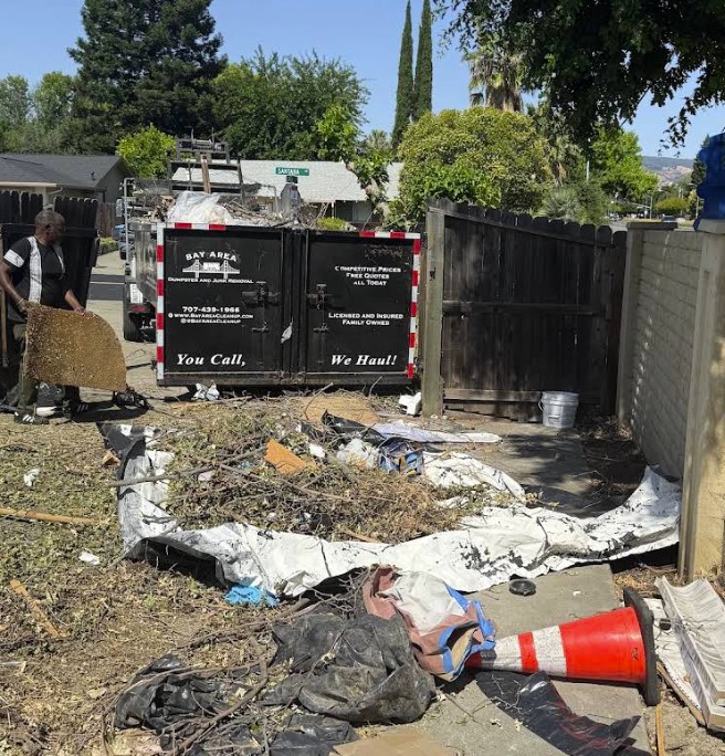 Crew clearing yard debris next to a Bay Area Dumpster branded bin